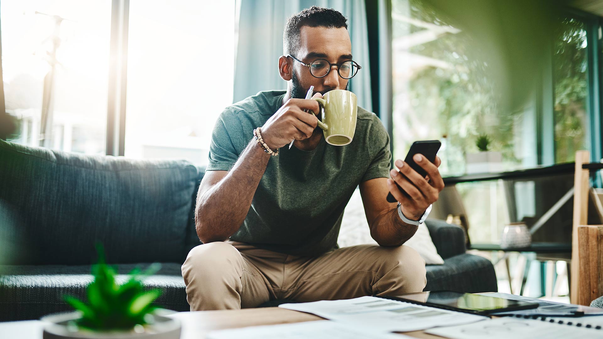 Man sitting on couch drinking out a cup looking at his phone